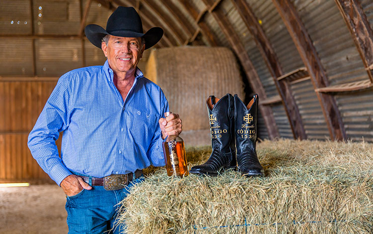 George Strait poses next to a hay bale with his Cotigo tequila.